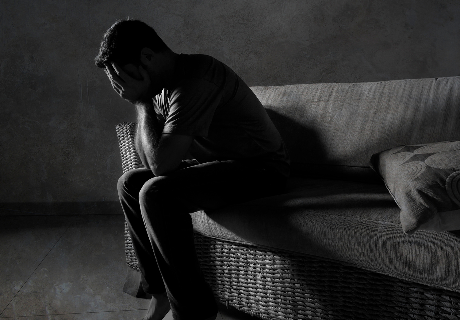 A black and white portrait of young sad and depressed man sitting on a couch with his head in his hands