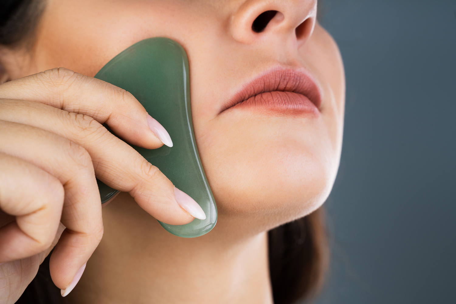 a woman using a gua sha massage tool on her face