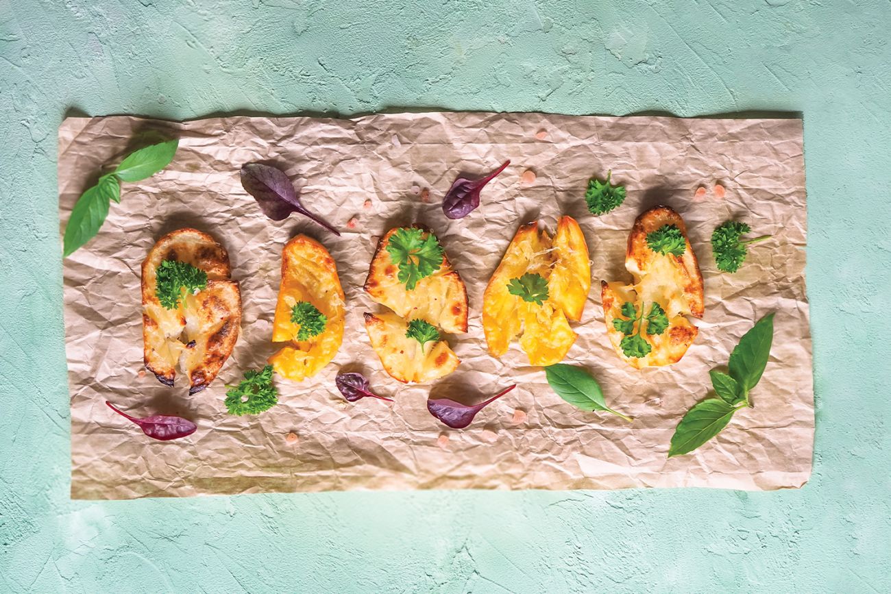 Crispy potatoes on parchment paper garnished with herbs and greens on a light blue background.