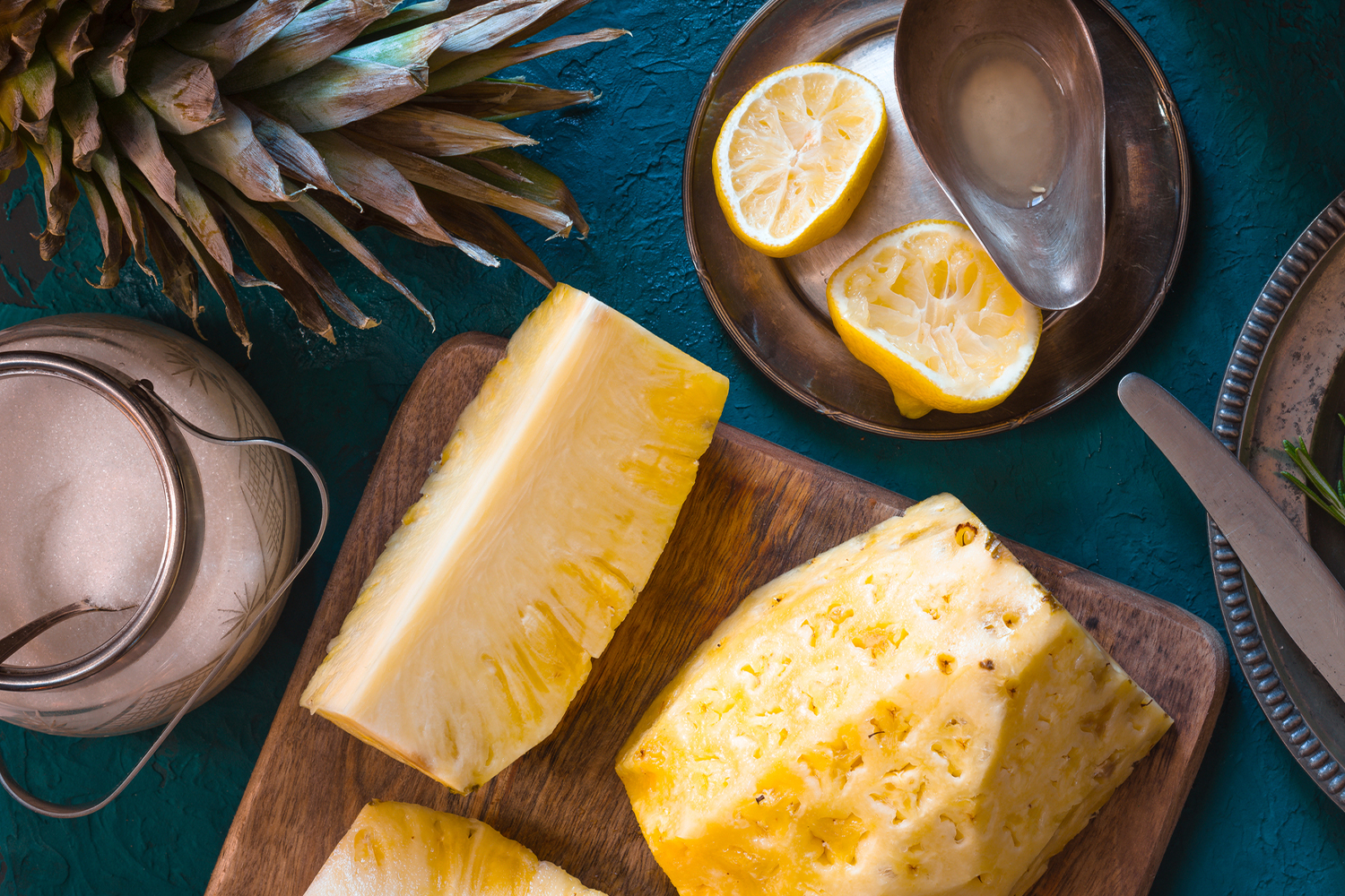  Pineapple on a cutting board with sliced lemons and a jar of sugar on a dark blue background.