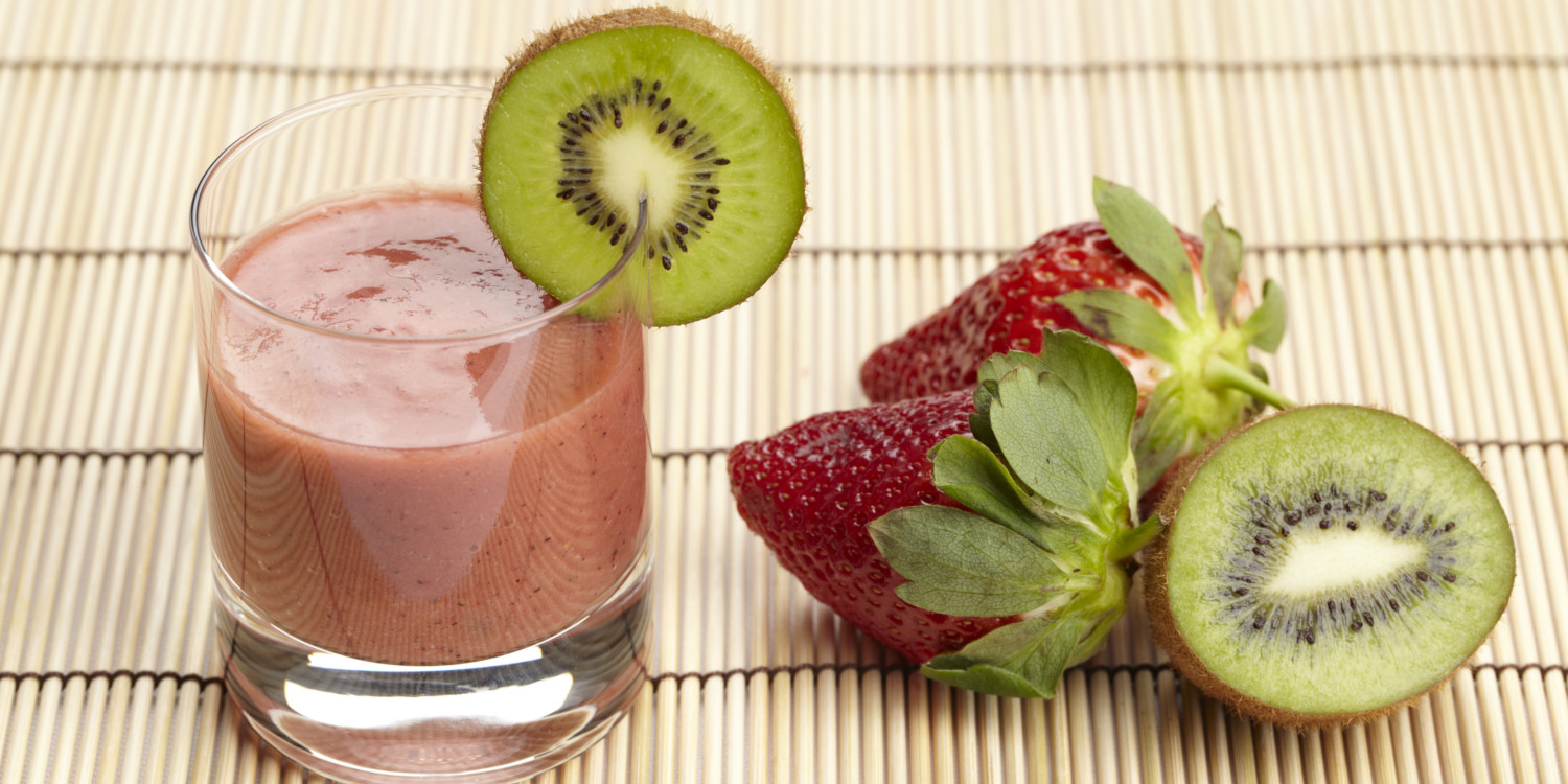 a glass of smoothie next to fresh strawberries and kiwi