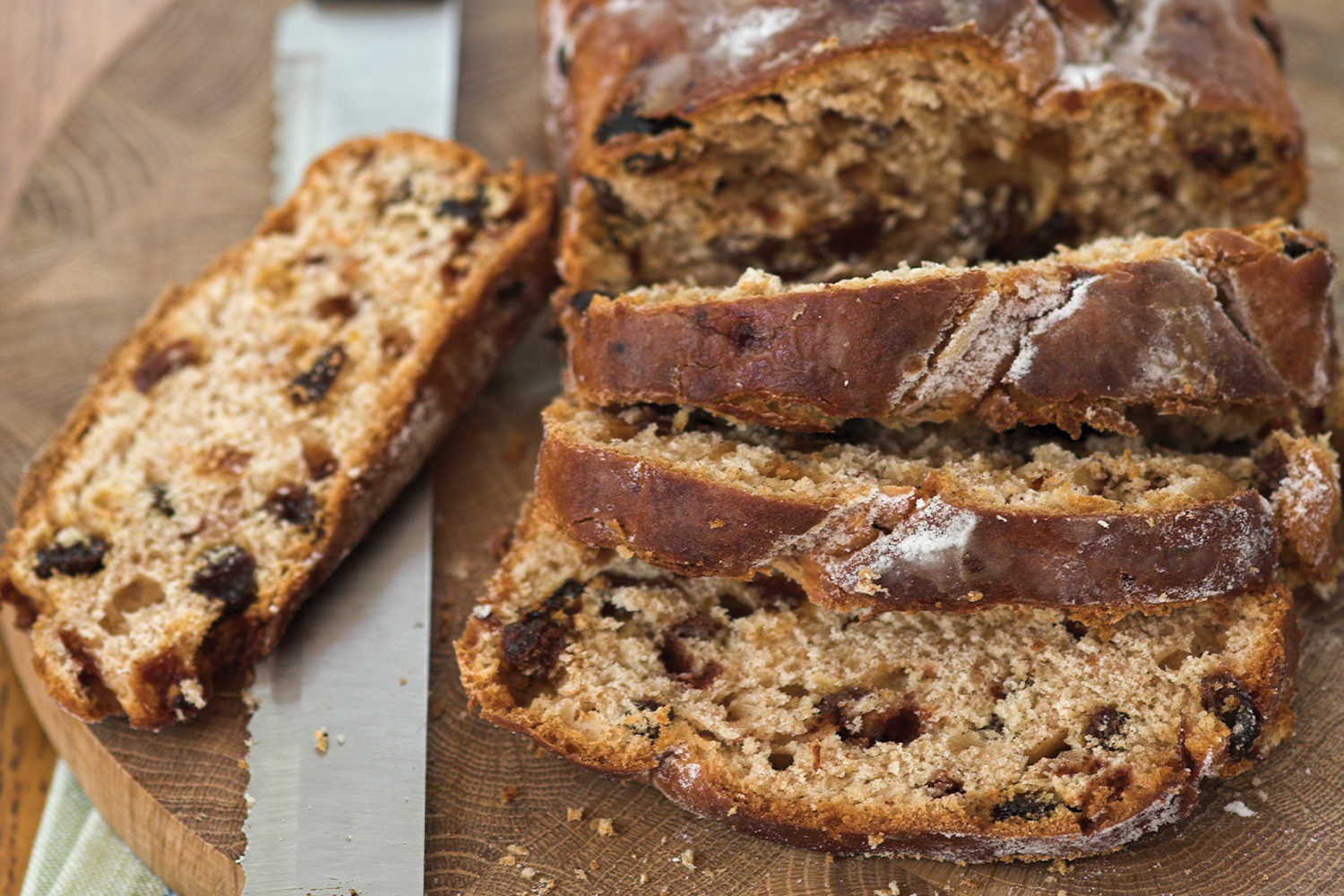 Walnut & Raisin Loaf sliced on a round wooden cutting with bread knife.
