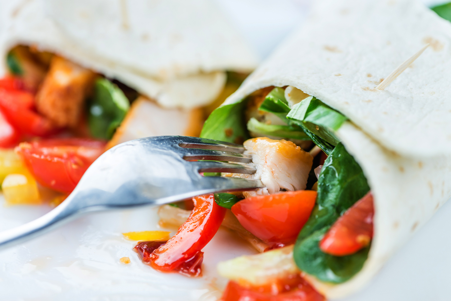 a fork snagging a piece of diced chicken from inside a wrap sandwich