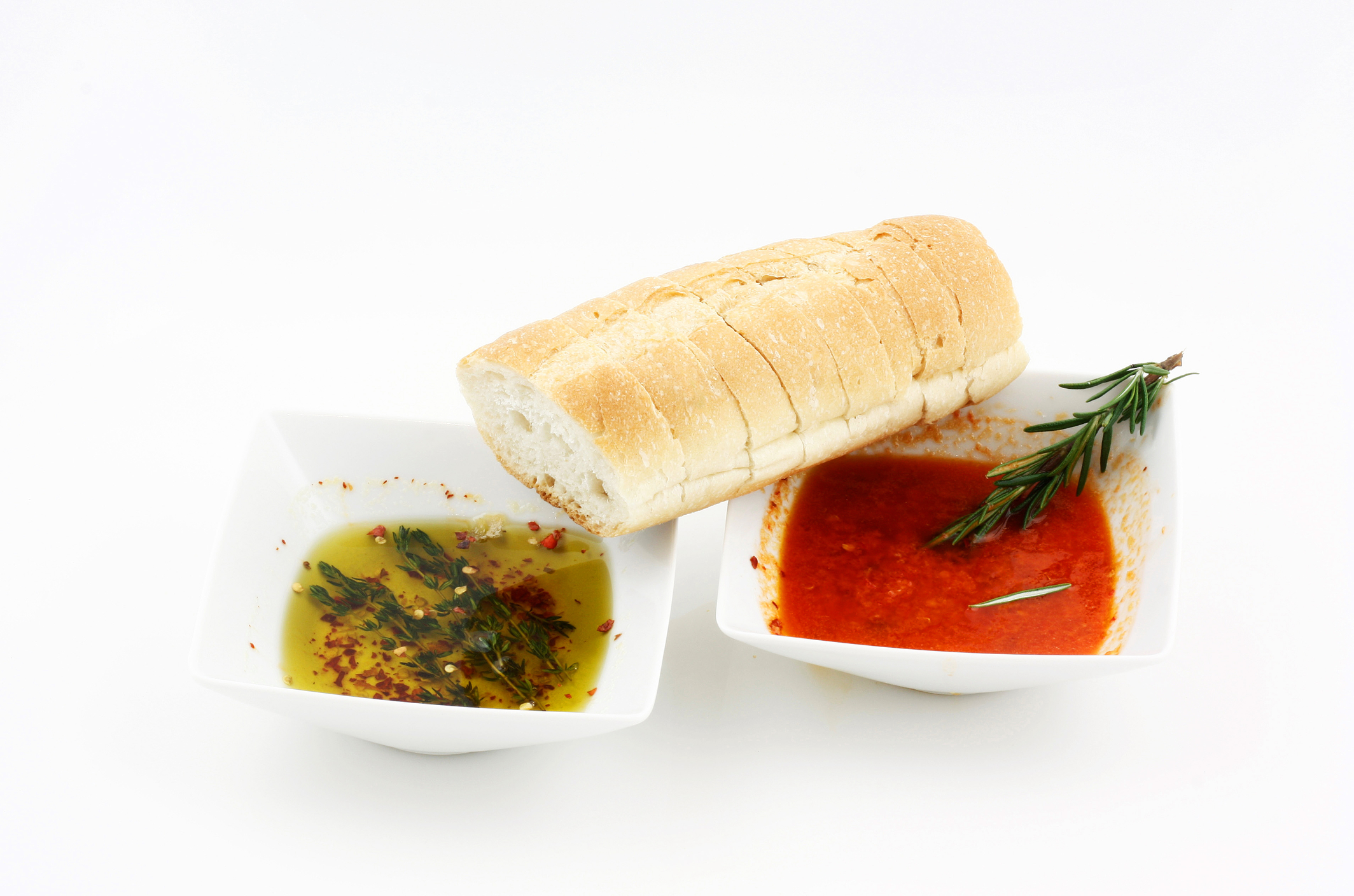 Crusty bread with two types of dipping bowls, one filled with golden oil, the other with a red oil.