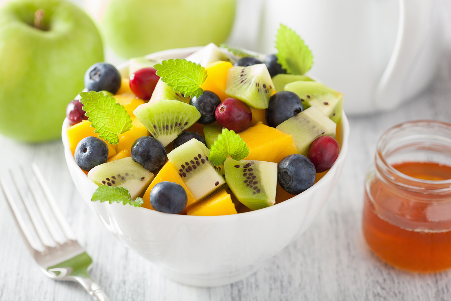 a bowl of kiwi, melon, blueberries, and grapes, with a honey sauce