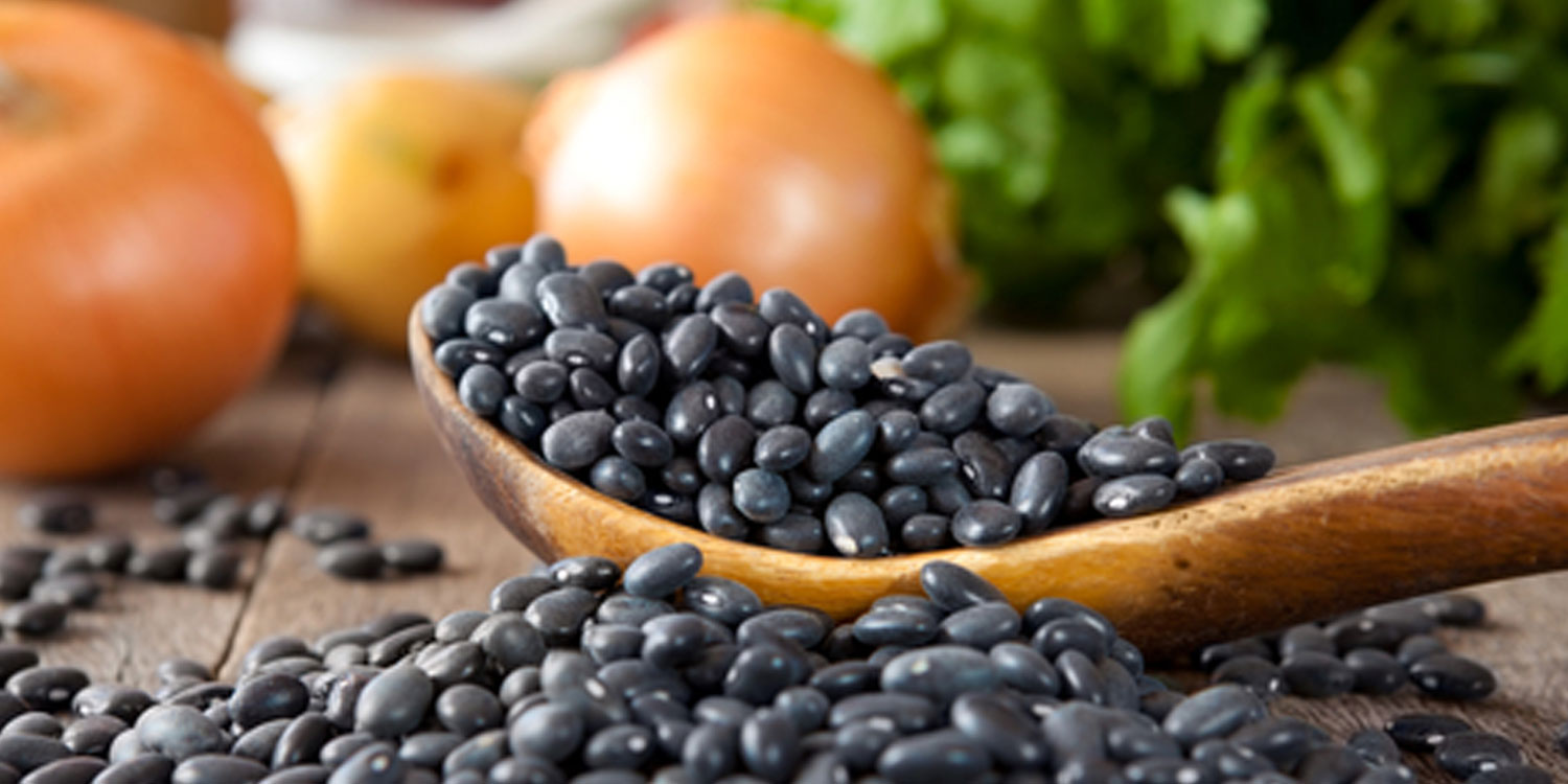 Black beans in wooden spoon, wooden table and onion in background.
