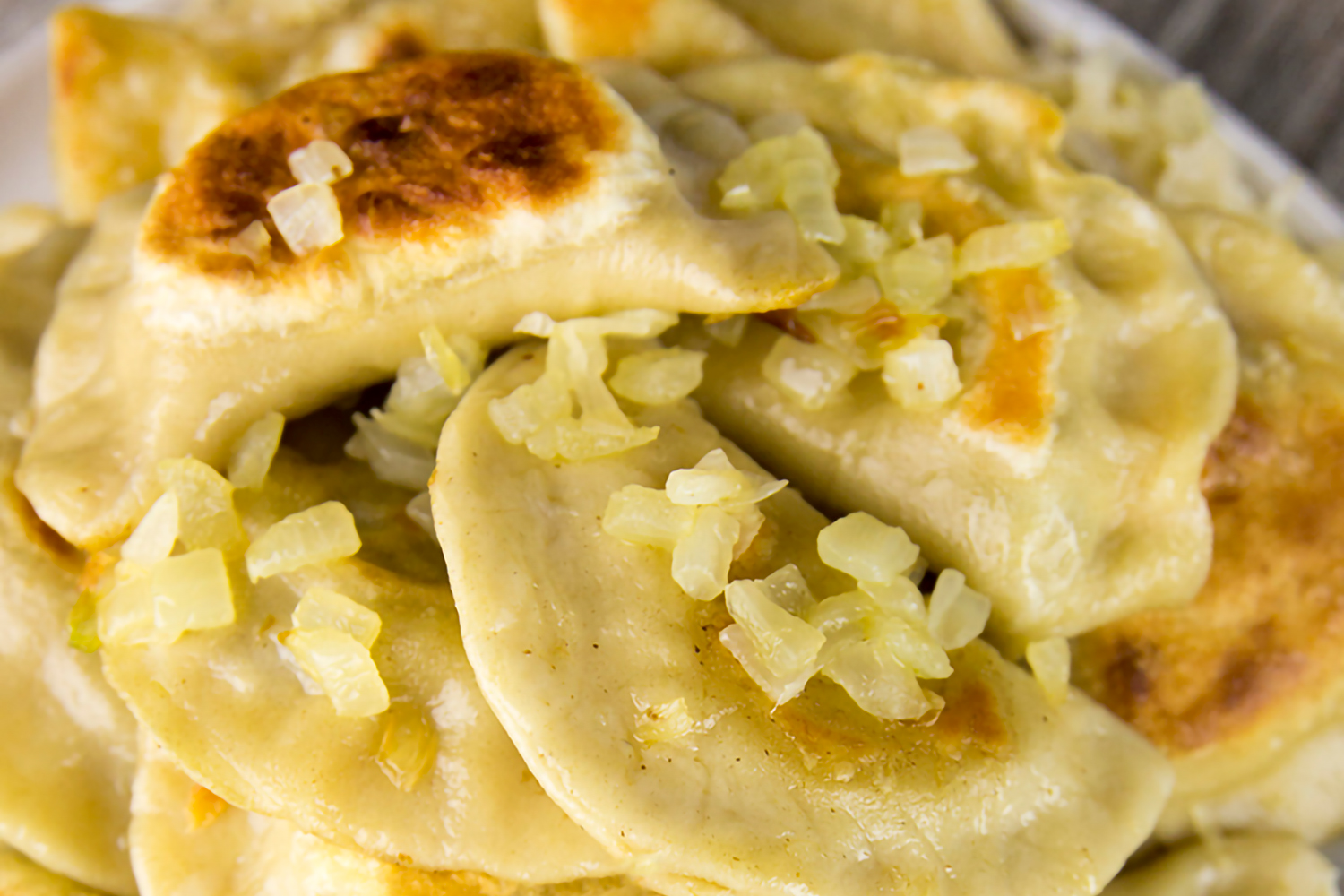 a plate piled with fresh pierogi topped with saurkraut