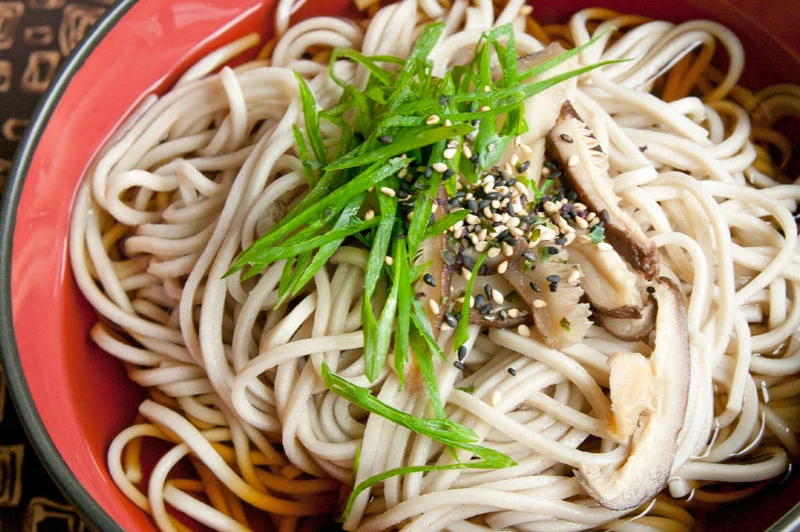 a bowl of soba noodles garnished with sesame seeds and scallions