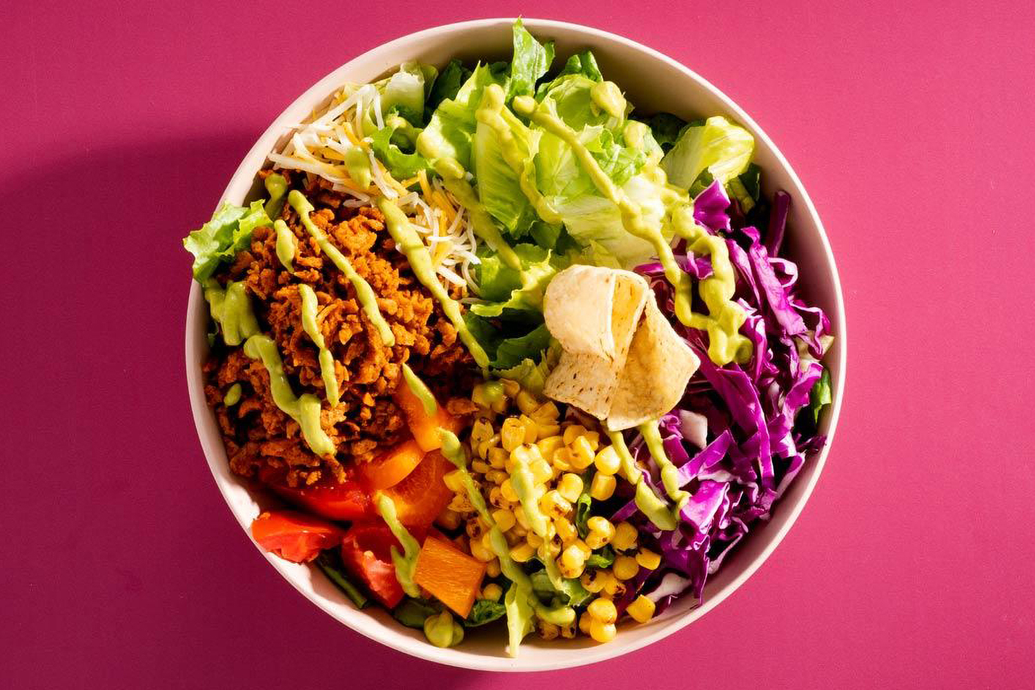 a bowl of lettuce, corn, peppers, and vegan taco filling