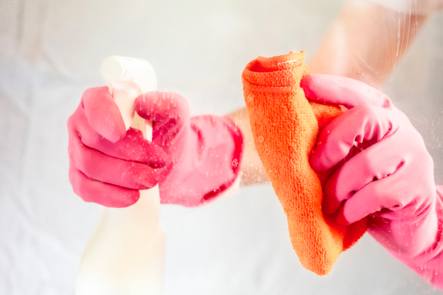 Hands with rag and spray bottle cleaning glass.