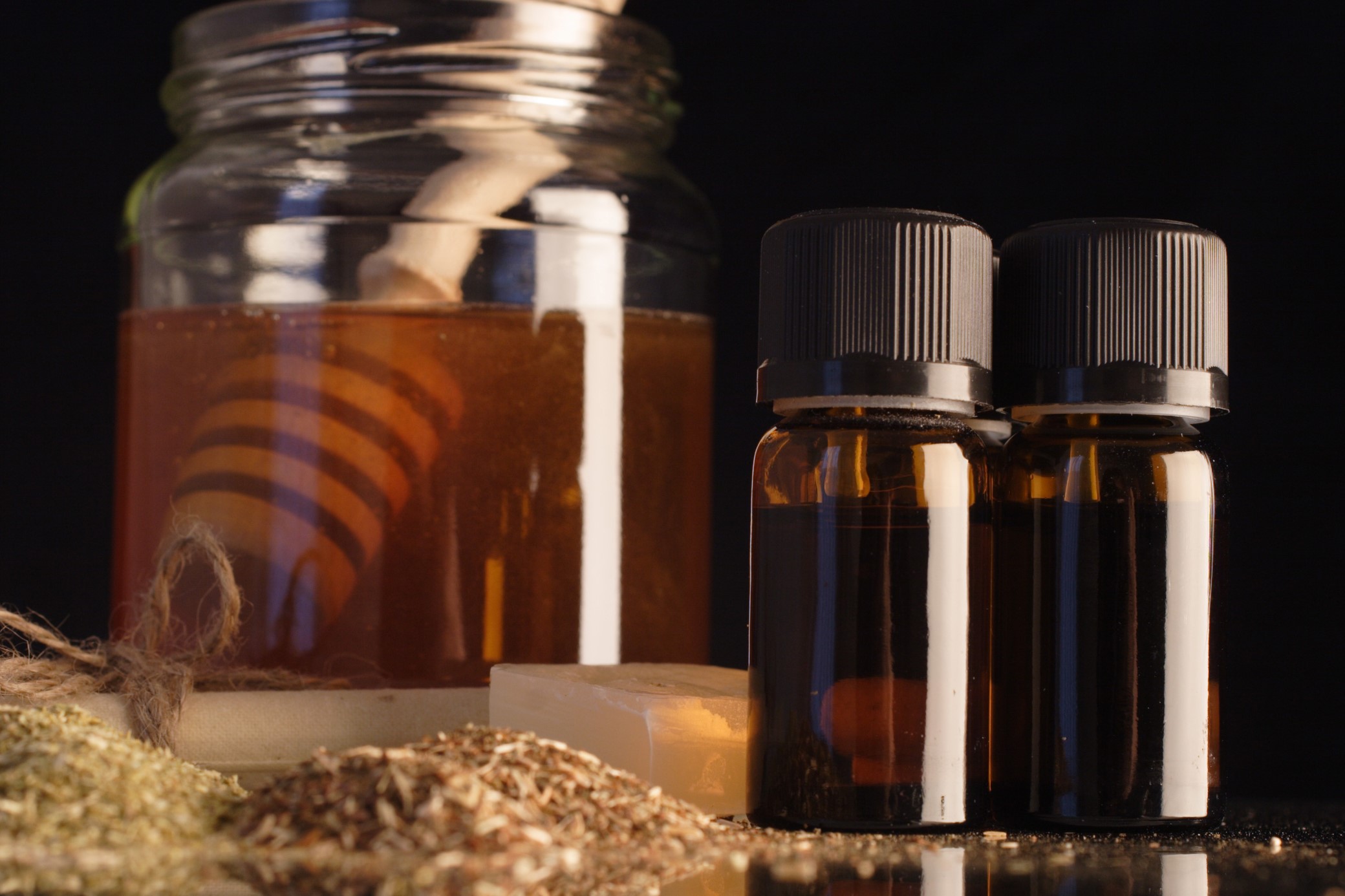 A jar of honey with essential oil bottle against a black background.