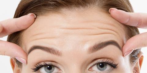 a woman checking the skin on her face for wrinkles