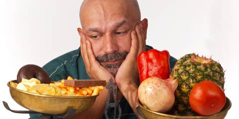 a disappointed man weighing fruits and veggies against fried food