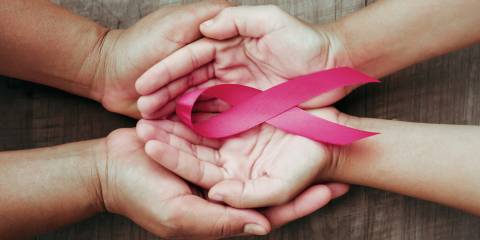 A larger pair of hands cupping a smaller pair of hands palms up with a pink breast cancer awareness ribbon.