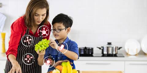 A mother and son i n the kitchen selecting fruits with icons of probiotic bacteria.