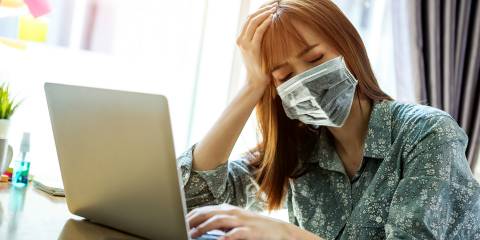 a fatigued woman in a mask working from home