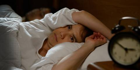 a restless woman in bed staring at the alarm clock