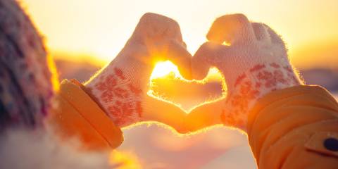 A woman's hands in knitted winter glove making a heart symbol.