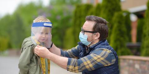 a masked man putting a face shield on his son