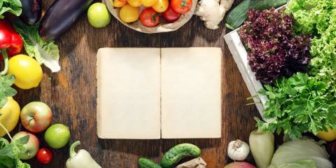 A blank notebook on a rustic table surrounded by fruits and vegetables.