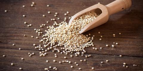 A scoop spilling quinoa out onto a wooden table.
