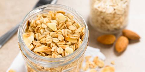 Coconut Almond granola in glass jar, ingredients and spoon in the background.
