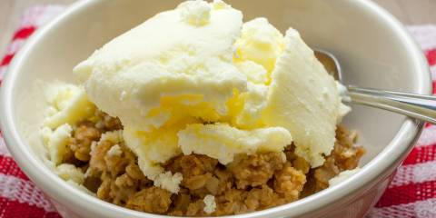 Homemade peach crisp in a white bowl and spoon.
