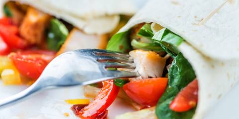 a fork snagging a piece of diced chicken from inside a wrap sandwich