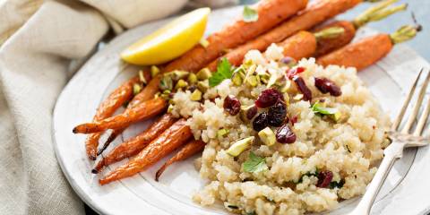 Quinoa salad with pistachios served on a white plate with roasted potatoes.