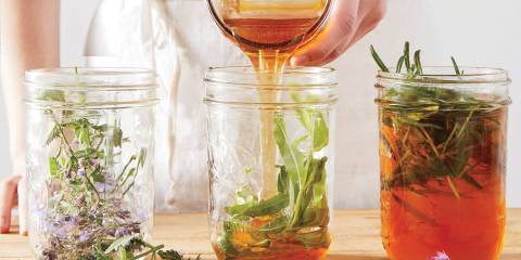 A woman in a white apron pouring honey into jars of herbs.