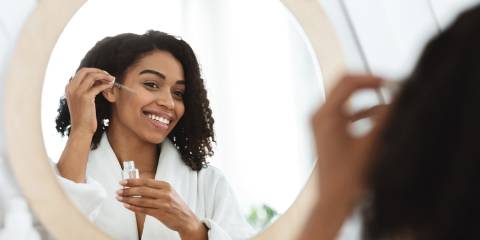 a woman applying oils to her face in the mirror