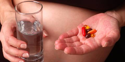Pregnant woman about to take vitamins with glass of water.