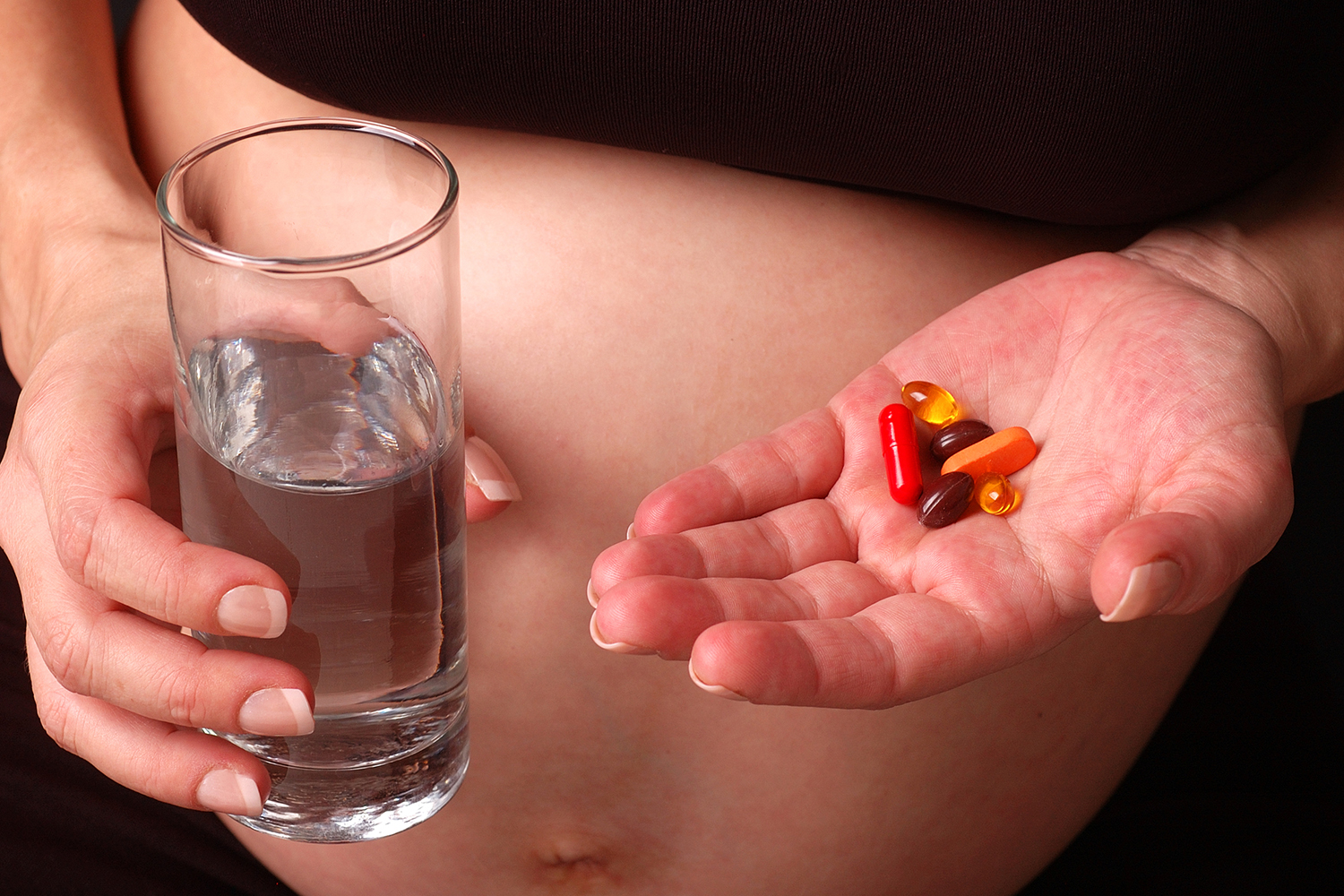 Pregnant woman about to take vitamins with glass of water.