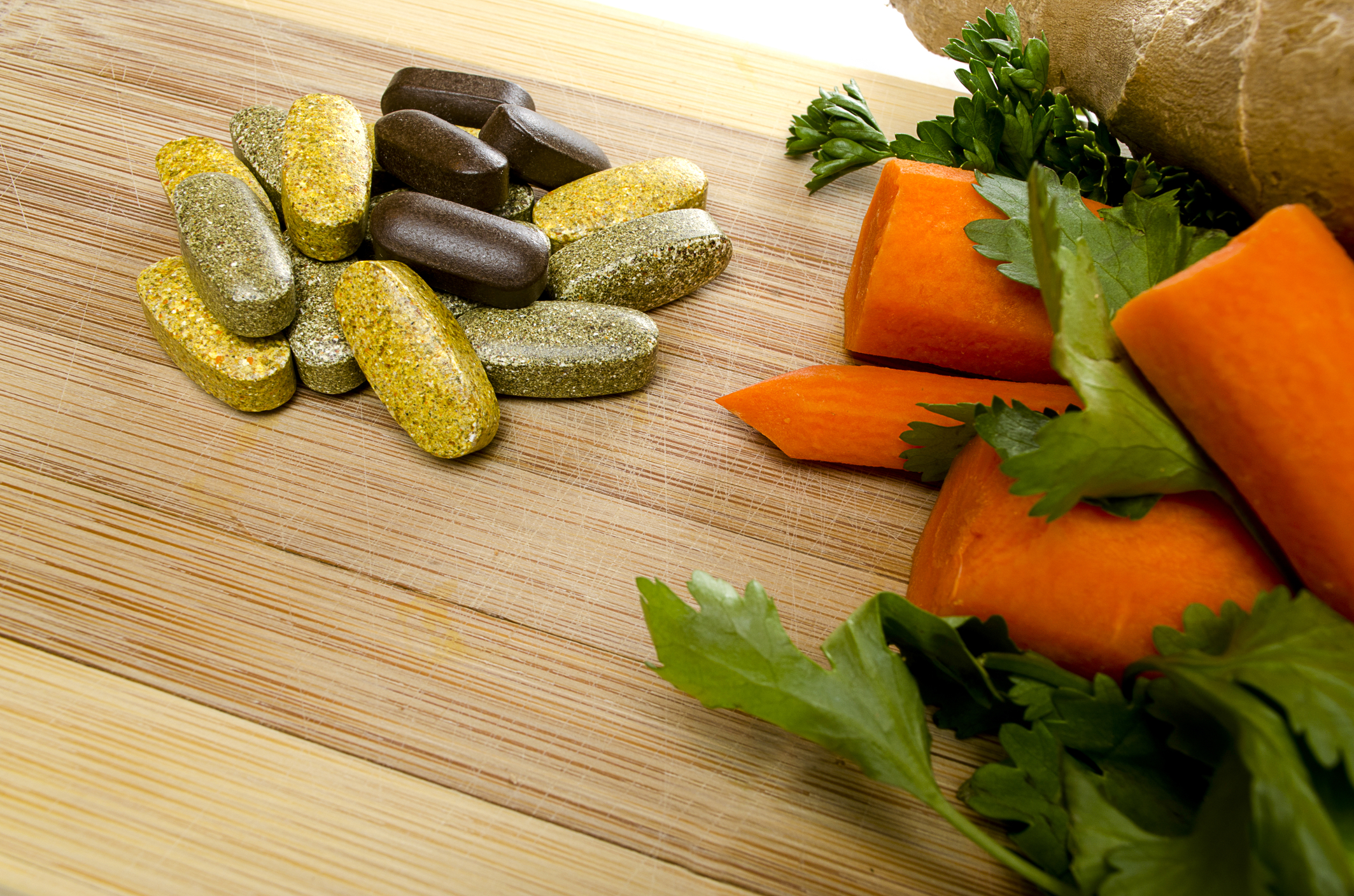 Vitamins next to some vegetables on a wooden table. 
